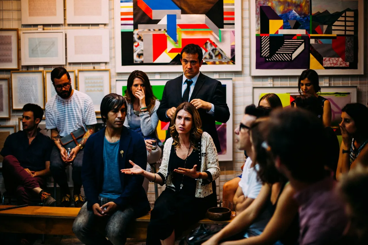 A group of people in a discussion in a room hung with paintings