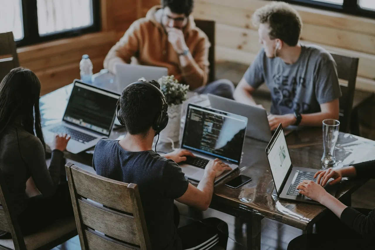 Five people working on laptops around a wooden table