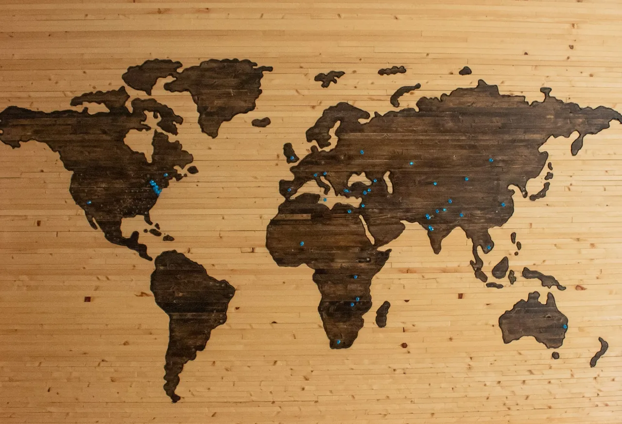 A wooden world map on a wall, marked with pins