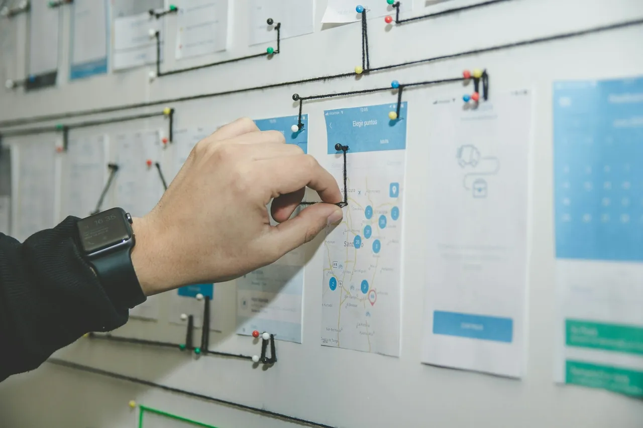 A hand pinning string between printed screens on a planning wall